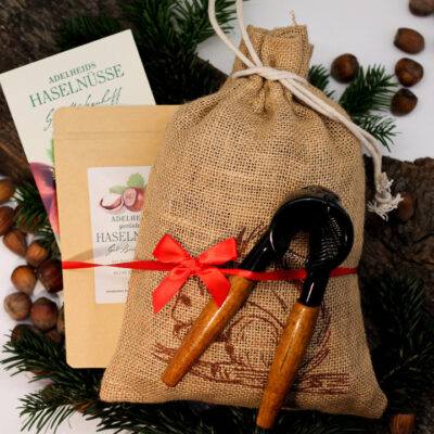 Jutesack mit roter Schleife, zwei Nussknackern, Haselnüssen und Haselnussverpackungen auf Tannenzweigen