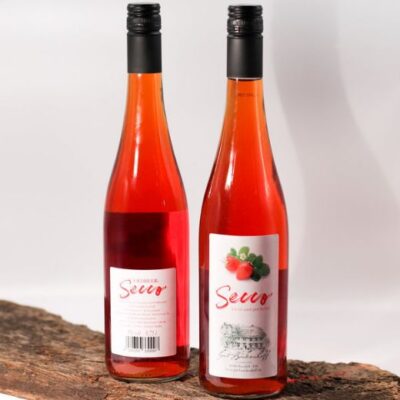 Zwei Flaschen roten Secco mit Erdbeer- und Himbeerabbildungen stehen auf einem Holzbrett