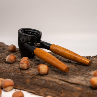Schwarzer Nussknacker mit Holzgriffen und mehreren Haselnüssen auf einem Holztisch