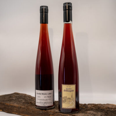 Zwei Flaschen roter Likör auf einem Holzbrett: links Cordial Medoc Likör, rechts Raesfelder Schlossgeist